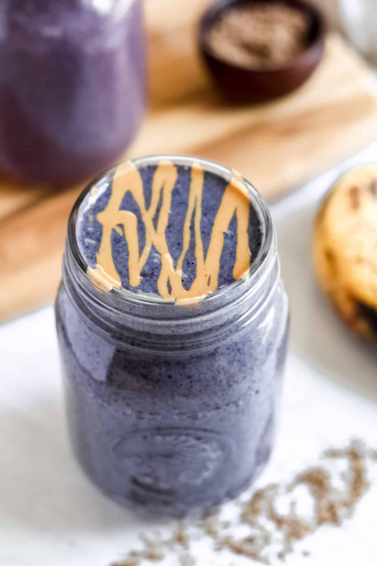 Purple-colored Blueberry Banana Peanut Butter Smoothie served in a mason jar, with a drizzle of peanut butter on top.