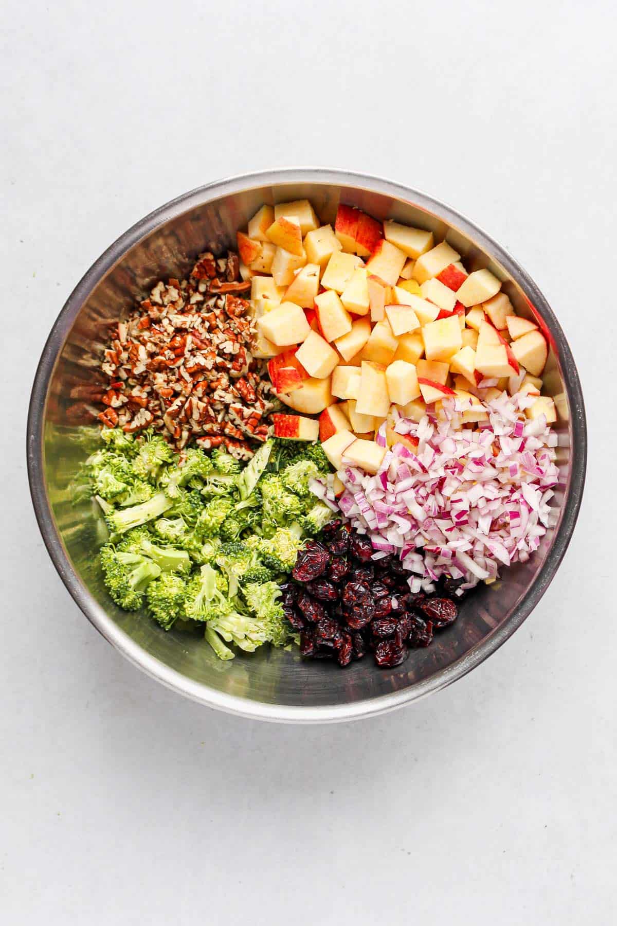 Individual ingredients for vegan broccoli apple salad arranged in a large stainless steel bowl, ready to be mixed together.