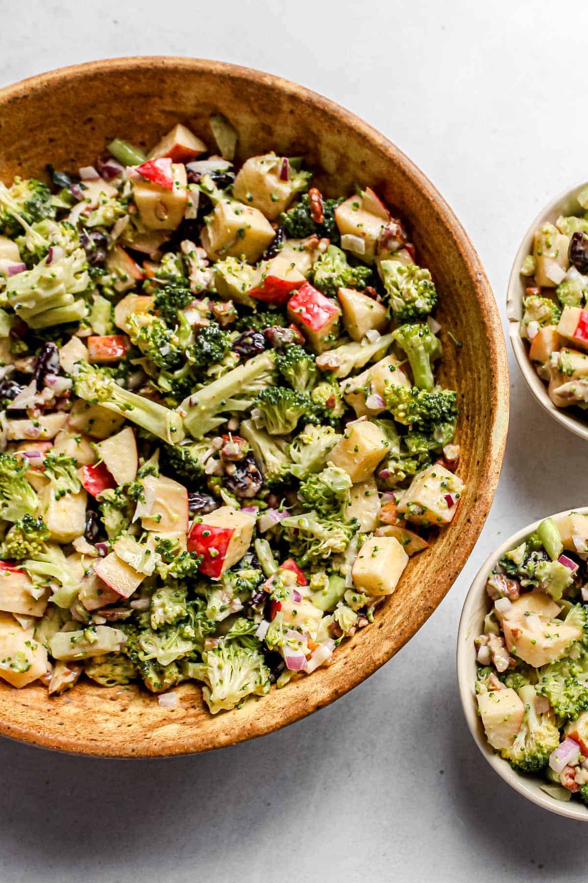 Large ceramic bowl with creamy plant-based broccoli apple salad, accompanied by two smaller individual bowls, ready for serving.