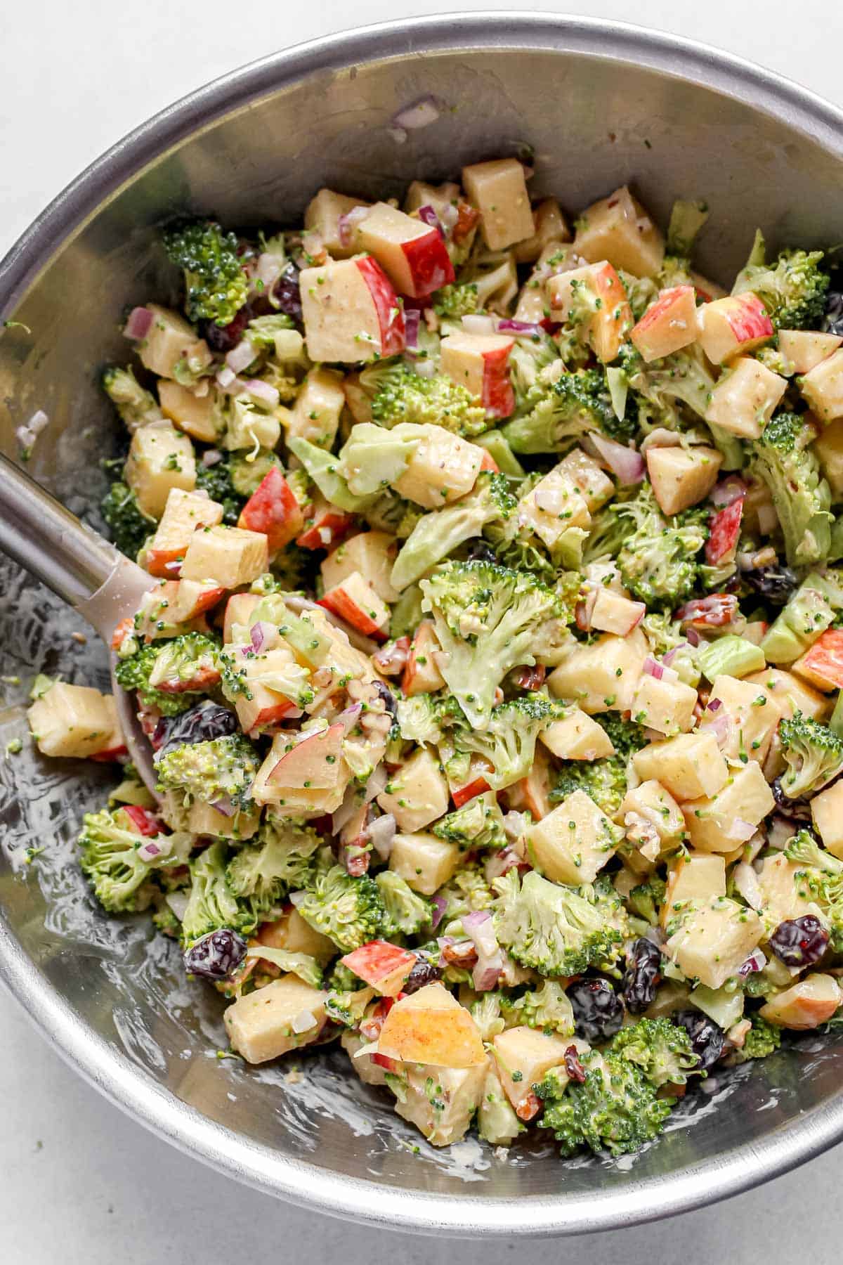 A large spoon mixing the creamy dressing into the broccoli and other ingredients, ensuring everything is evenly coated.