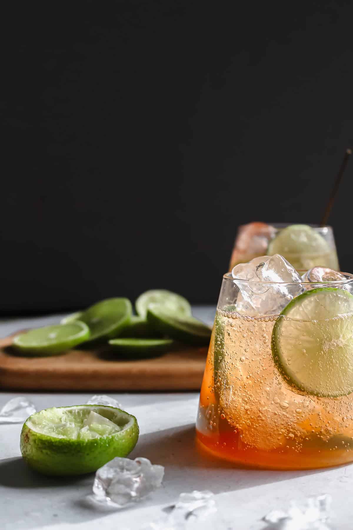 A glass of soda water, bitters, and lime next to a half of a lime that has been juiced.