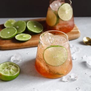 Two glasses of Bitters and Soda with Lime with sliced limes on a serving board