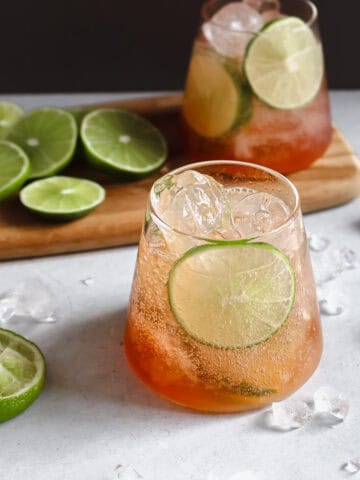 Two glasses of Bitters and Soda with Lime with sliced limes on a serving board