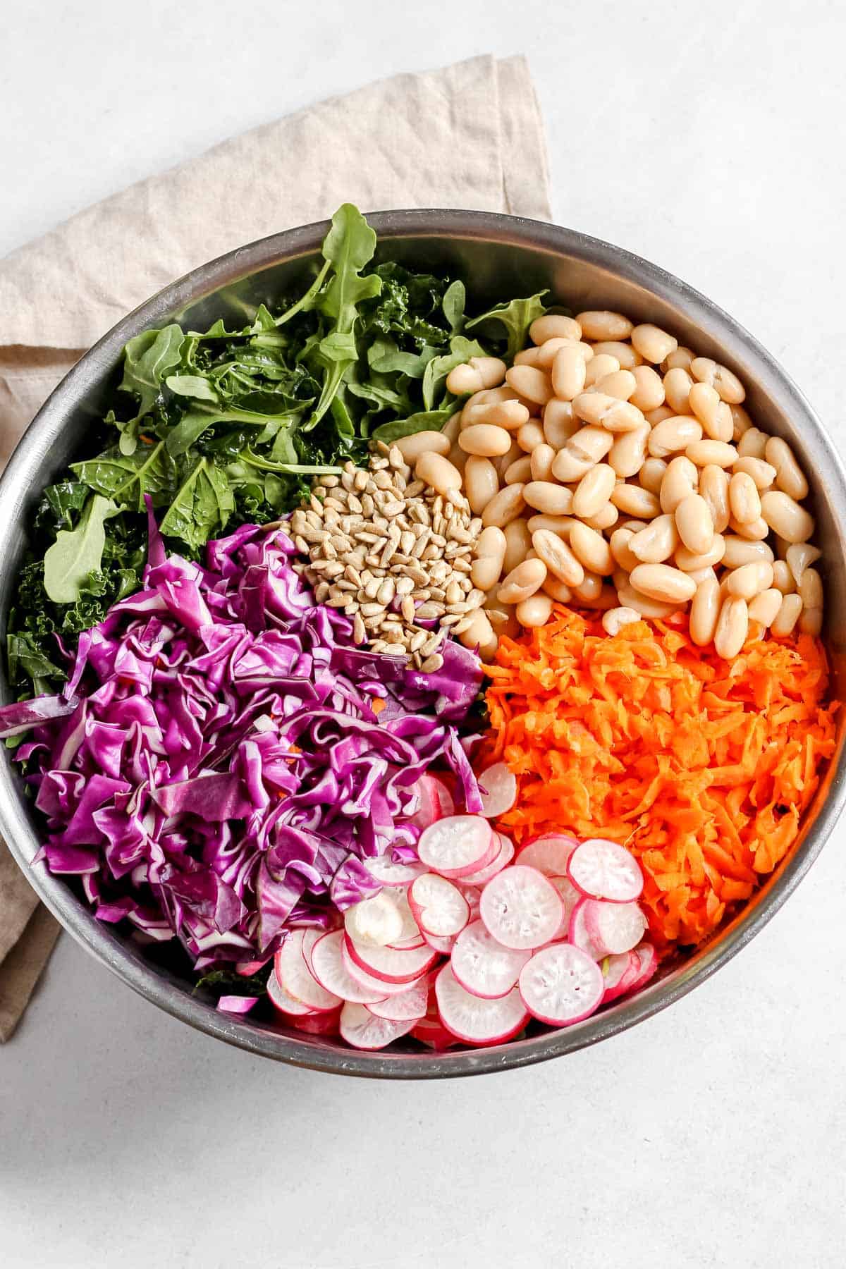 Large stainless steel bowl filled with individual salad ingredients on white background.