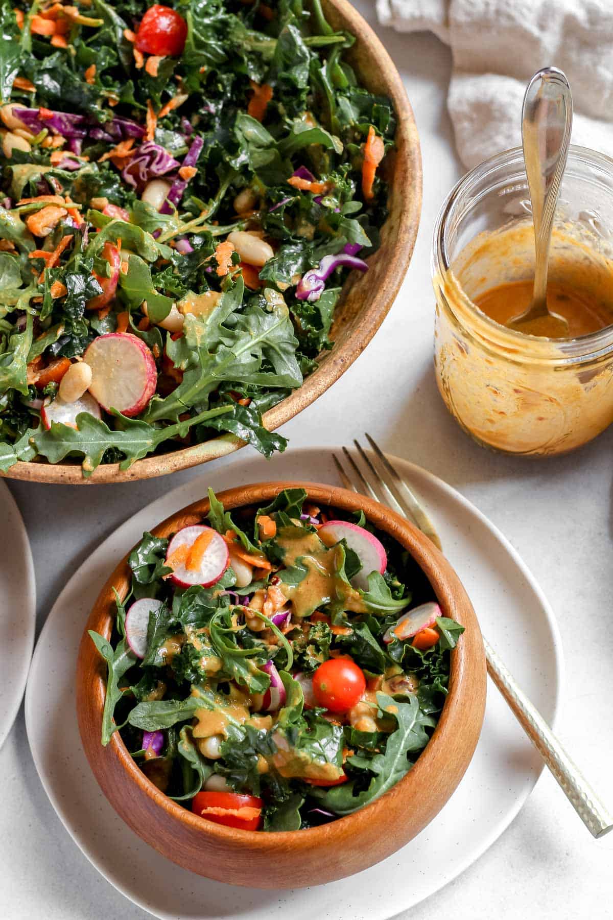 Salad with dressing drizzled on it served in wooden bowl on white background.