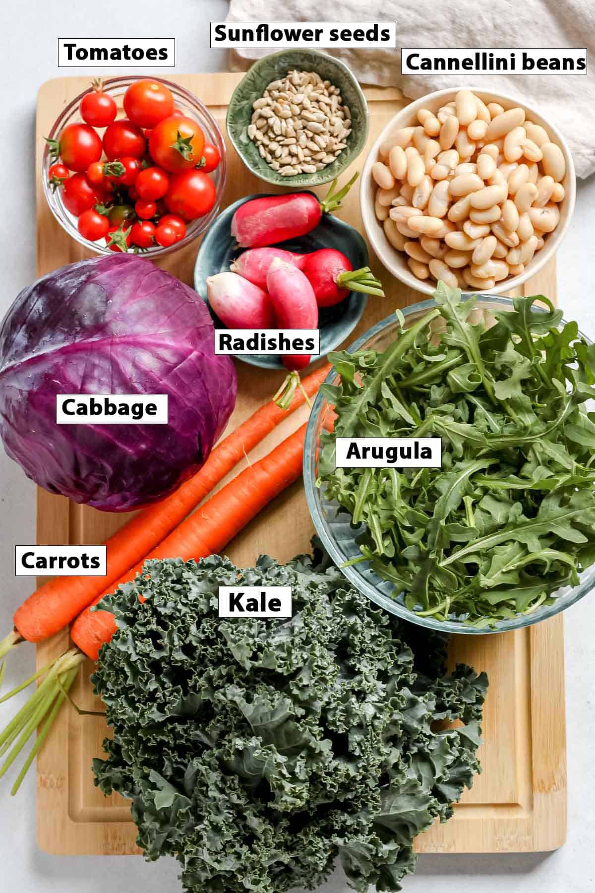 Individual salad ingredients on a wooden cutting board.