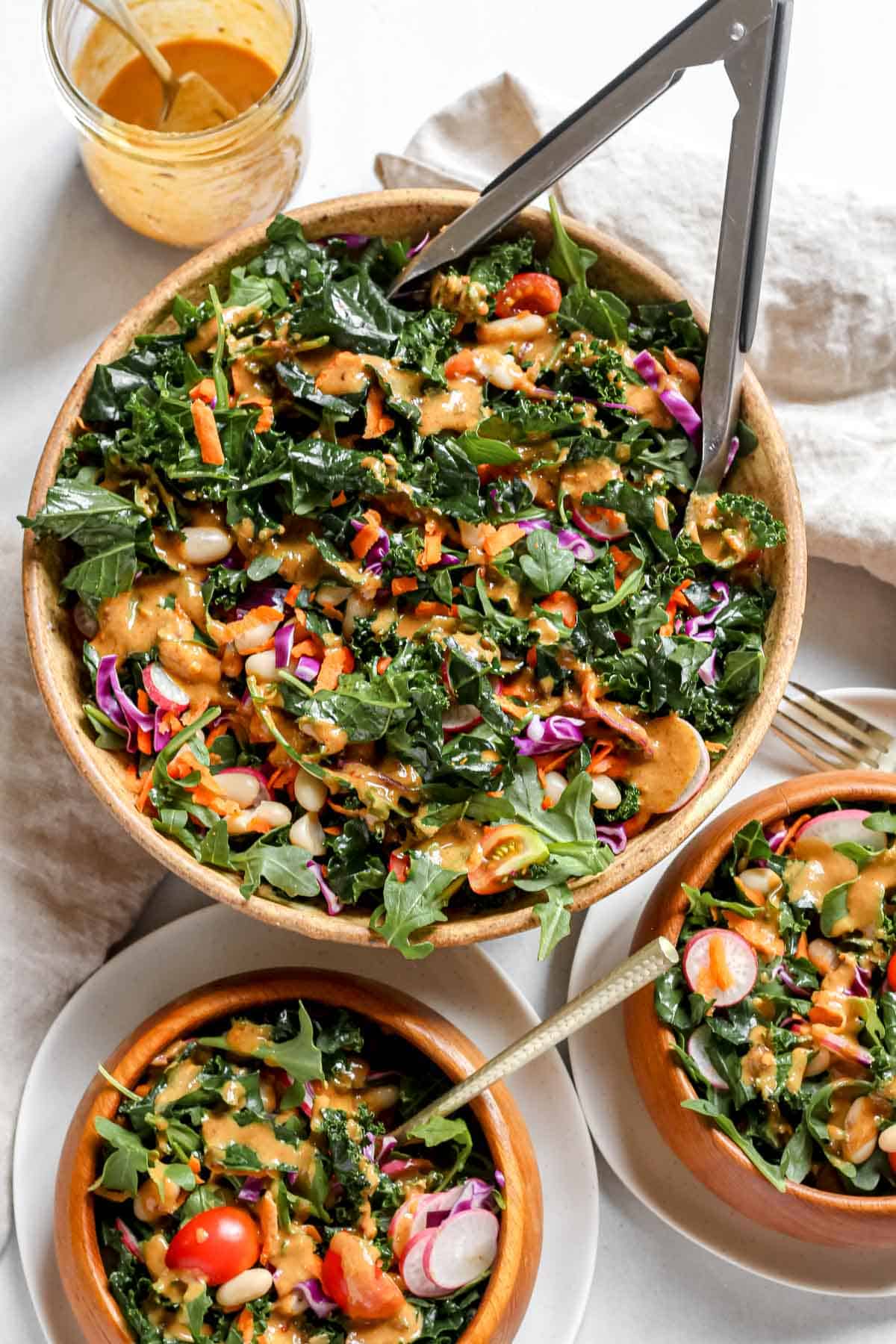 Dressing drizzled on a colorful salad that is served in bowls on a white background.
