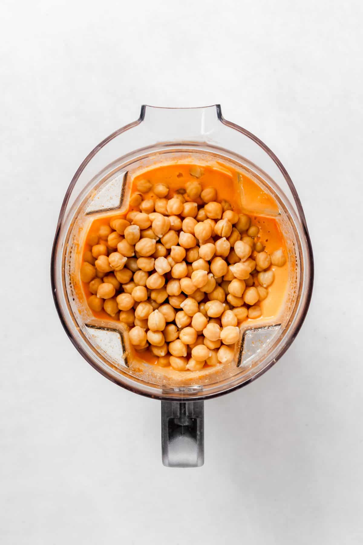 Adding chickpeas to blender with sauce already in it on white background