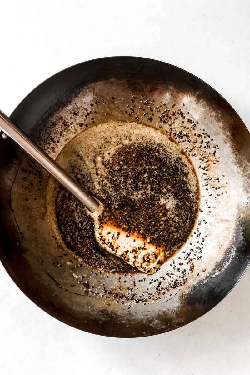 Steel wok filled with the sauce, garlic, sesame seeds, and spices and a spatula.