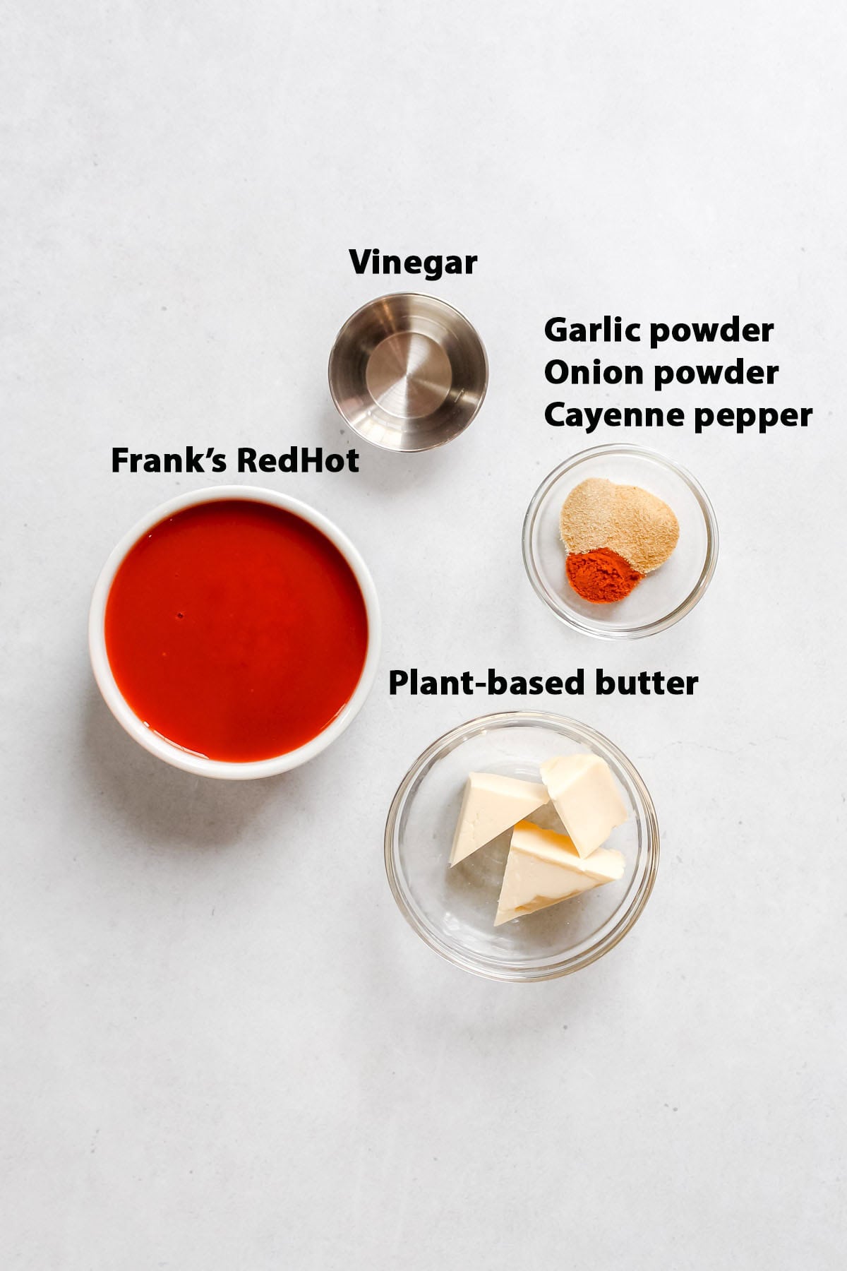 Individual ingredients: Frank's RedHot sauce, spices, and plant-based butter in individual bowls on a white background.