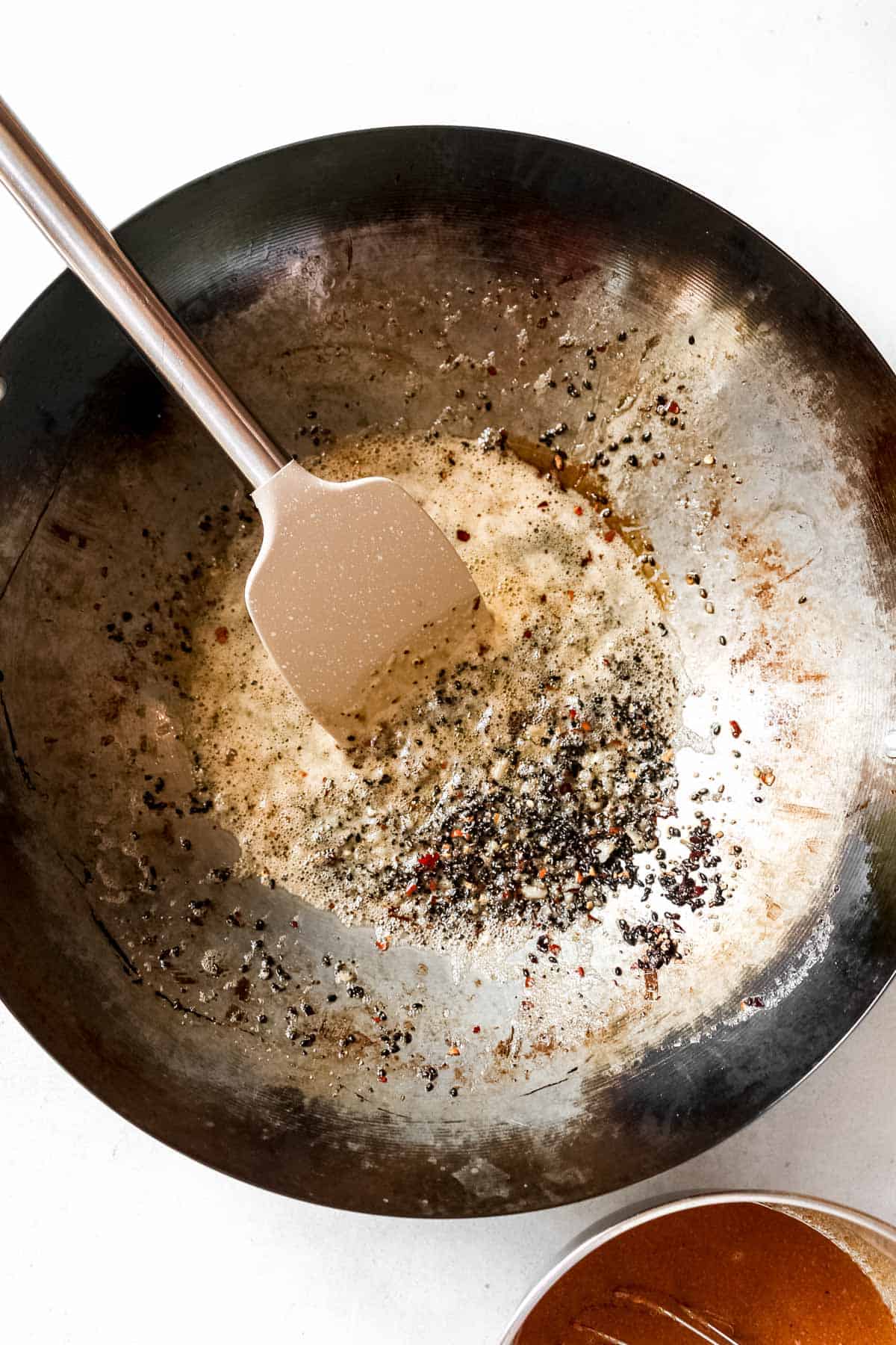 Wok with sesame oil, garlic, sesame seeds, red pepper flakes, and black pepper.