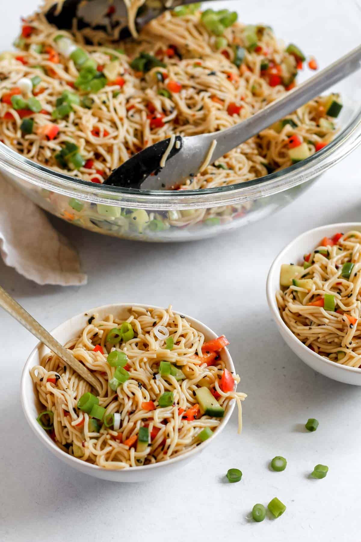 A large glass bowl of the finished sesame noodles along with 2 smaller white serving bowls filled with noodles and a fork.