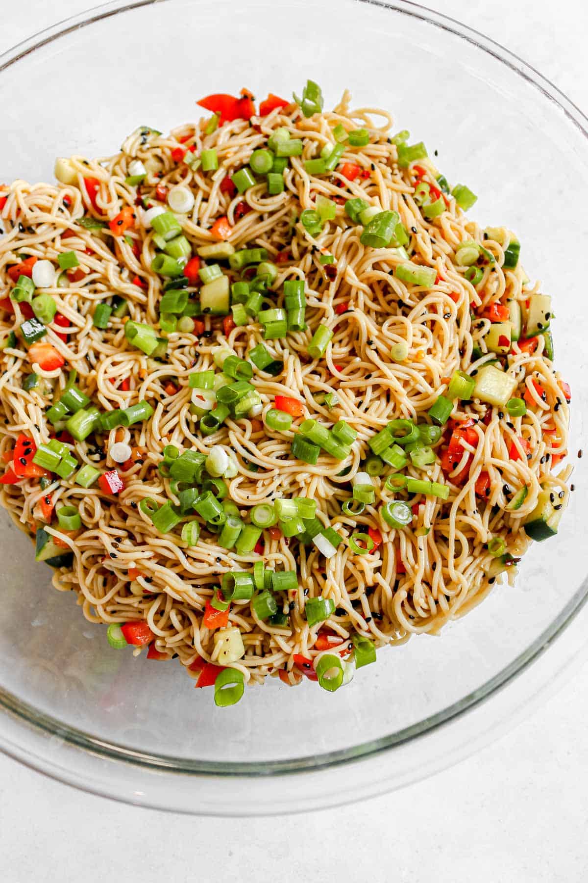 Cold sesame noodles in a large glass bowl topped with green onions