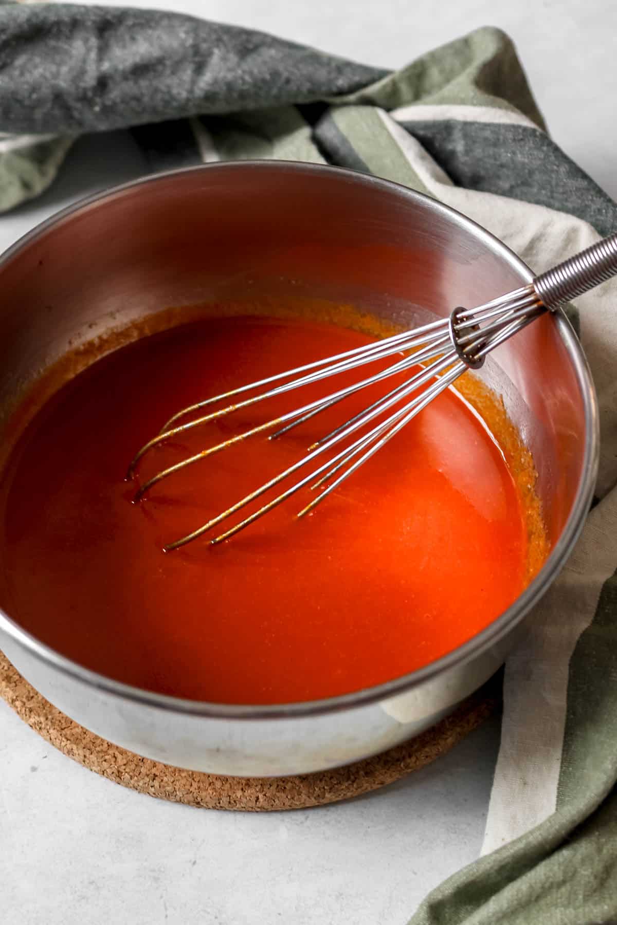 Whisking in spices, RedHot sauce and vinegar in a stainless steel pan.
