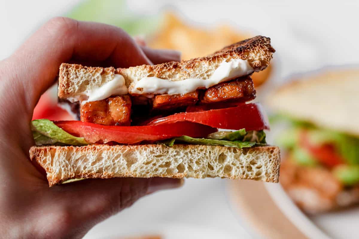 Hand holding half of vegan tempeh lettuce and tomato sandwich