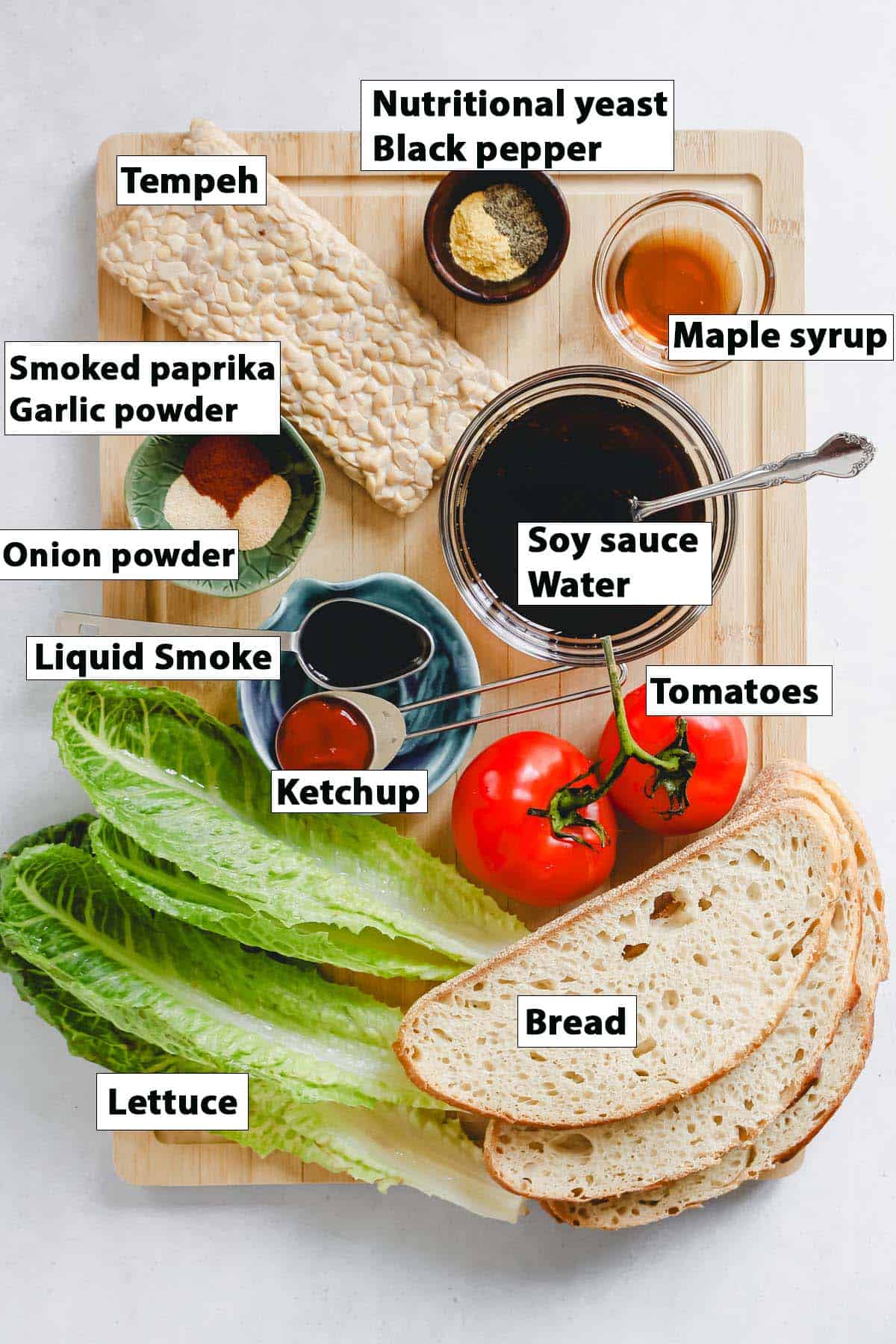 Individually labeled vegan BLT ingredients on wooden cutting board on a white background