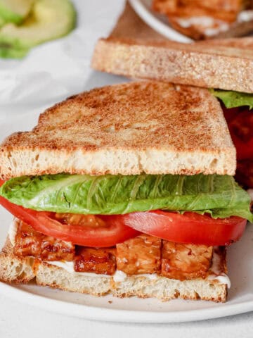 Sandwich containing tempeh bacon, lettuce, tomato and vegan mayonnaise on a white plate